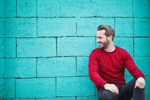 man wearing red sweatshirt and black pants leaning on the wall