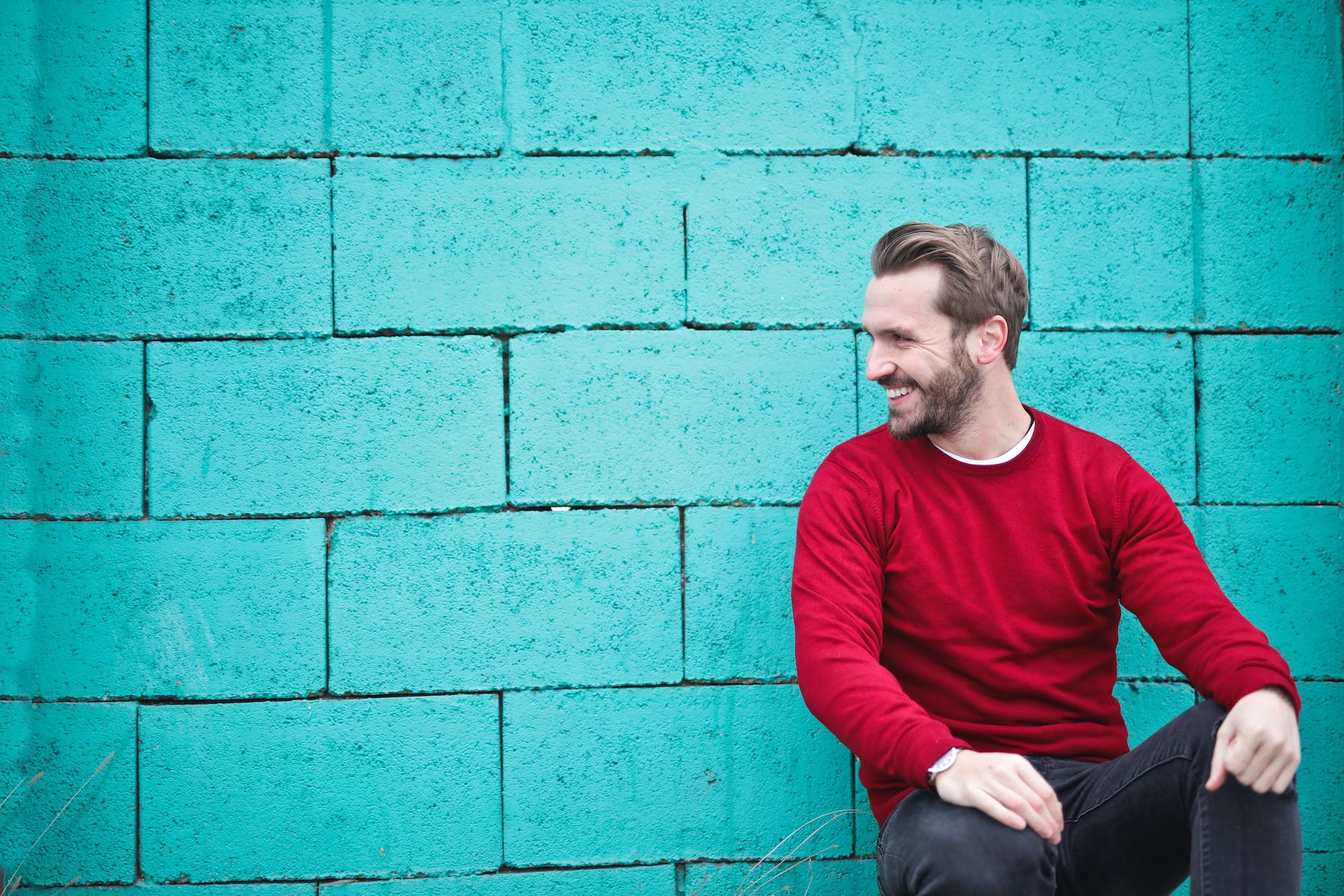 man wearing red sweatshirt and black pants leaning on the wall